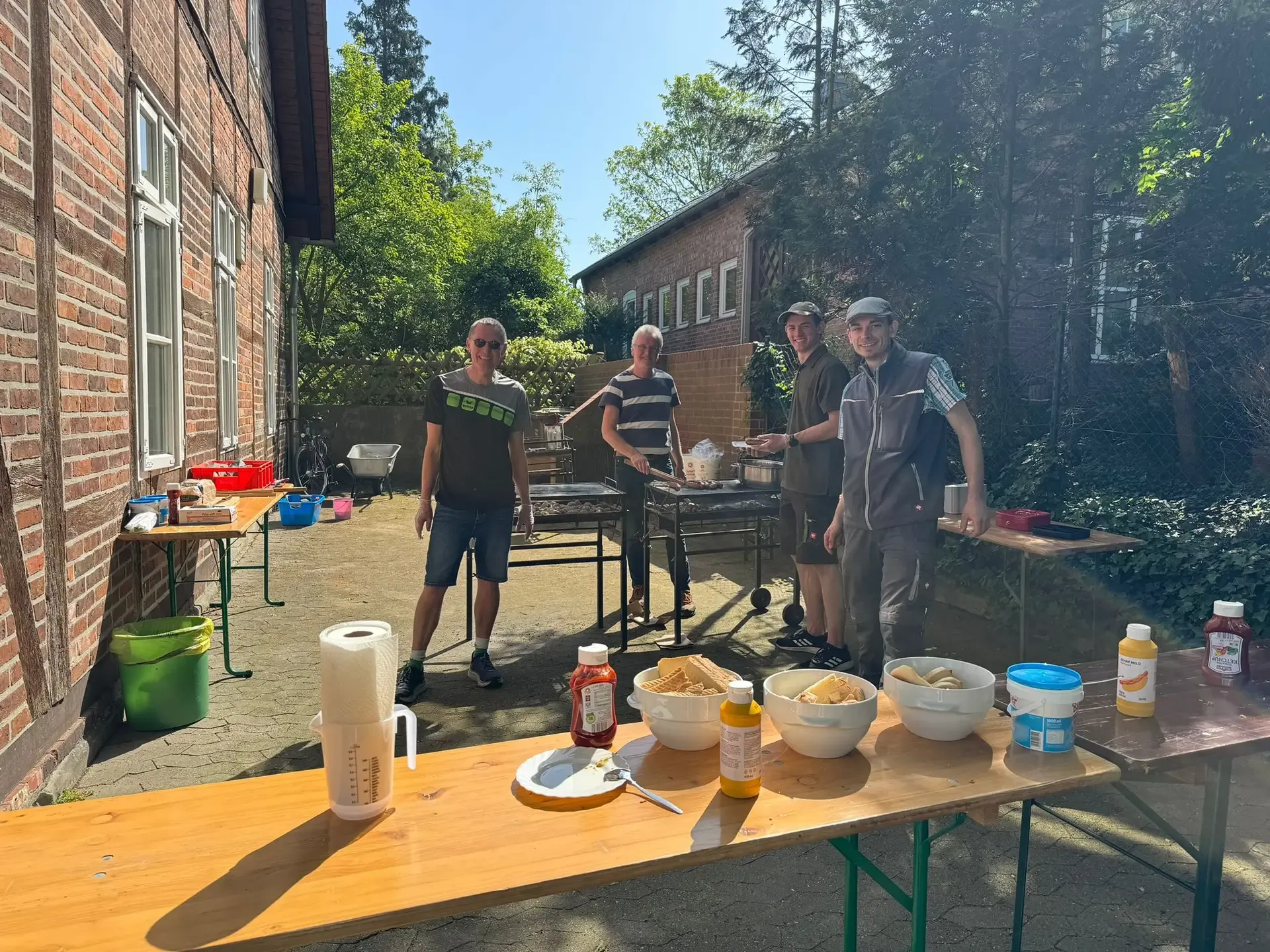 Vier Personen am Grill hinter einem gedeckten Tisch im Hof